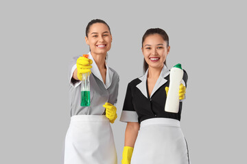 Poster - Young chambermaids with cleaning supplies on light background