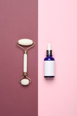 Wall Mural - Massage roller and serum bottle for anti-aging facial massage on a pink burgundy background