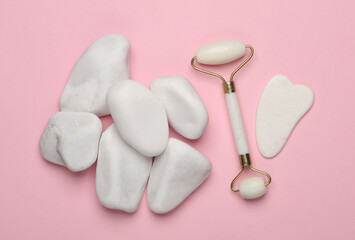 Wall Mural - Massage roller and gua sha scraper for anti-aging facial massage, pebbles on pink background