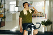 © DragonImages - A man drinking water from a bottle after an intense workout session on a stationary bike at home