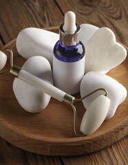 Wall Mural - Jade facial roller and gua sha scraper, serum bottle,  pebbles on wooden background. Beauty concept.