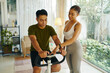 © DragonImages - A man and woman working together to adjust the settings on a stationary bike in a modern living room