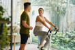 © DragonImages - A man and woman smiling at each other during a workout session with the woman on a stationary bike