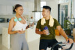 © DragonImages - A man and woman hydrating with water bottles after an exercise session in a stylish, modern living room