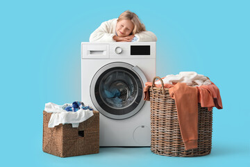 Canvas Print - Little girl sleeping on washing machine near baskets with laundry against blue background