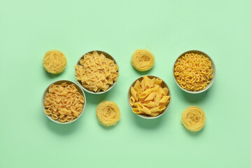 Wall Mural - Bowls with different tasty uncooked pasta on green background