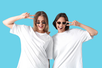 Sticker - Female friends in sunglasses showing victory gesture on blue background