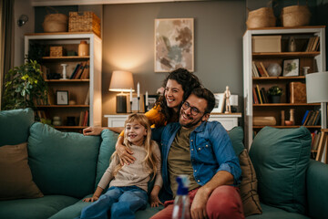 Wall Mural - Smiling parents with their daughter enjoying quality time on the living room sofa