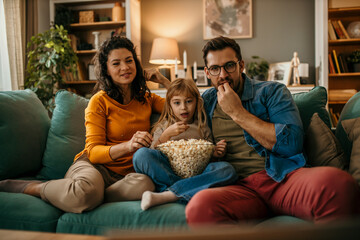 Wall Mural - A family od three watching with a contained emotion a tv during the day in the living room