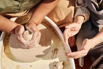 Top view closeup of two women creating ceramics together at pottery wheel lit by sunlight copy space