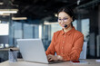 © Liubomir - Asian woman with headset phone smiling working inside office with laptop, online customer support worker, businesswoman typing on keyboard, solving and helping customers remotely, successful woman.