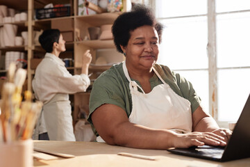 Wall Mural - Portrait of African American senior woman using computer in art studio and managing small business copy space