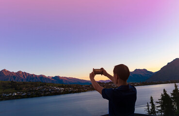 Wall Mural - Young tourist man backpack using smartphone take picture at View of landscape sunset  scene in Queenstown ,New zealand