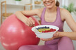 © Studio Romantic - Cropped portrait of a young sporty cheerful slim woman wearing sportswear eating healthy food after working out at home sitting on the floor with fit ball. Healthy nutrition and lifestyle concept.