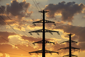 Silhouettes of high voltage towers with electrical wires on background of sunset sky and dark clouds. Electricity transmission lines, power supply concept