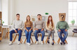 © Studio Romantic - Confident smiling people job candidates and seekers wearing casual clothes sitting in a row with unknown faceless man in paper bag on head with question mark. Employment and recruitment concept
