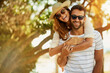 © peopleimages.com - Couple, portrait and smile on piggyback in outdoor with lens flare for summer holiday and fun in Bali. Relationship, people and happy for support on vacation, trip and travel together with sunglasses