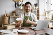 © sofiko14 - Adult bearded male potter engaged in e-commerce selling handmade clay products on Internet. Happy worker in apron holds unique bowl created in personal style against background of shelves with dishes.
