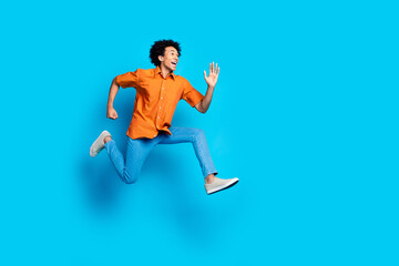 Wall Mural - Full length photo of handsome excited guy wear orange shirt jumping high running emtpy space isolated blue color background