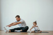 © standret - Teaching how to stretch the legs. Father with little daughter are doing yoga at home