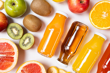 Assortment of fruit juices in glass bottles among fruits on white background top view