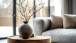 © john - Close up of ceramic vase with blossom twigs on round wooden coffee table against grey sofa and window. Minimalist home interior design of modern living room.