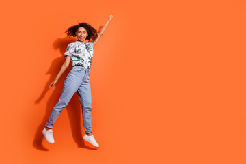 Poster - Full body photo of american woman in jeans and summer stylish shirt jumping overjoyed superhero isolated on orange color background