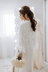 Wall Mural - A woman in a white gown stands in front of a mirror, holding a bouquet of white roses. Concept of elegance and sophistication, as the woman is dressed in a wedding gown