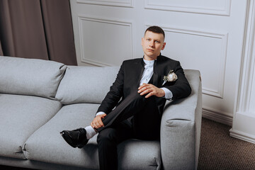 Wall Mural - A man in a suit is sitting on a couch. He is wearing a tie and has a flower in his lapel