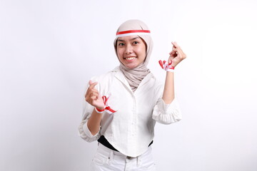 A young veiled Asian muslim woman wearing a red white ribbon feels nationalism, shapes heart gesture expresses her love for Indonesia. Indonesia's independence day concept.