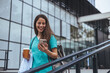 © Dragana Gordic - A cheerful female healthcare professional in teal scrubs enjoys a moment outside a medical facility, coffee in hand, as she navigates her smartphone.