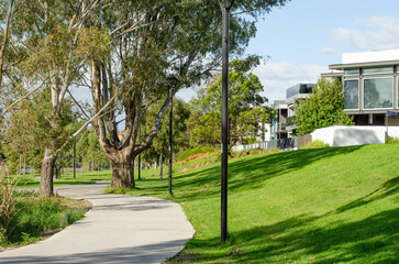 Wall Mural - A pedestrian walkway, footpath, or walking trail in a public green park with trees and grass, and some modern homes and houses nearby. A suburban local park in Maribyrnong, Melbourne, VIC, Australia.