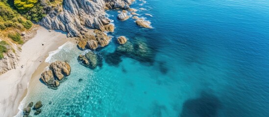 Poster - Top view of a sunny summer day seascape with a beautiful stone cliff, clear blue water, and a serene sea coast captured in an aerial drone shot