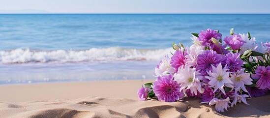 Poster - Flowers in shades of purple scattered on the sandy beach, with a clear sky above and the sea in the background, creating a serene scenery with copy space image.