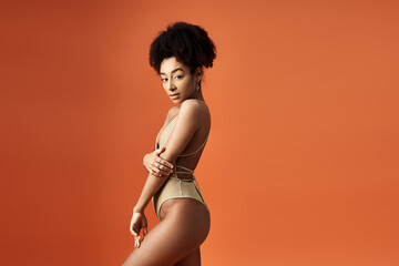 Poster - Stylish African American woman striking a pose in trendy swimsuit on bright orange background.