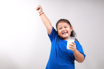 Adorable asian little girl standing while holding a glass of milk while making fist hand. Isolated on gray background with copyspace