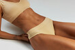 © Lustre Art Group  - Close-up of woman's toned midsection, highlighting her defined abs and beige ribbed lingerie against grey studio background. Concept of beauty and fashion, female health, anti-cellulite, dieting. Ad