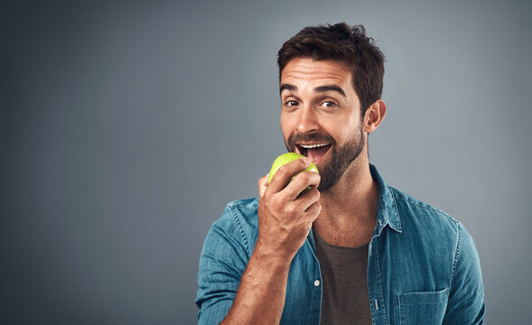 portrait, man and eating apple for nutrition, healthy diet or wellness isolated on gray studio backg