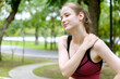 © gumpapa - young woman in sports bra touches her shoulder in pain or injury while jogging in a park at the morning. fitness, health, injury, exercise and outdoor activities.