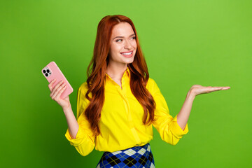 Wall Mural - Photo portrait of pretty young girl hold device hold look empty space wear trendy yellow outfit isolated on green color background