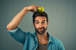 © peopleimages.com - Man, portrait and balance apple on head for healthy diet, wellness and natural organic food isolated on gray studio background. Fruit, face and person with nutrition target at breakfast for vitamin c