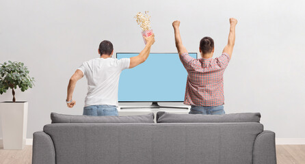 Wall Mural - Rear view shot of young men watching football match on tv and jumping from a sofa