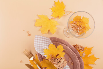 Wall Mural - Autumn table setting on beige background. Oval plates, cutlery, glass, checkered napkin and dry yellow leaves. Autumn holiday mood, Halloween, Thanksgiving concept. Top view, copy space