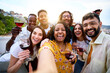 © CarlosBarquero - Selfie group of multiracial smiling friends enjoying at rooftop summer party holding glass of red wine. Happy community young people taking picture drinking alcoholic beverages on sunny day together