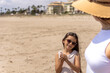 © pablo - A young girl with sunglasses smiles warmly at her mom while holding sand in her hands on a sunny beach day.