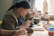 © AnnaStills - Side view of young woman with Down syndrome sitting at table in pottery workshop painting ceramic bowl, copy space
