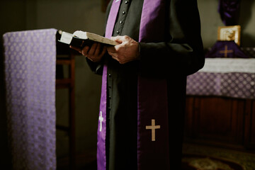 Poster - Crop shot of unrecognizable senior Catholic priest wearing soutane and stole standing indoors reading Bible