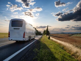 Wall Mural - white bus driving on the asphalt road in rural landscape at sunset