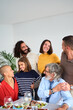 © CarlosBarquero - Vertical. Portrait of smiling Caucasian people looking affectionately at each other embraced together indoor at home. Multi-generational love family gathered at lunch table having fun at weekend
