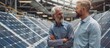 © Bolustck - A middle-aged man and his son, wearing business casual attire with jeans underneath, standing in front of solar panels at the factory's interior area.
